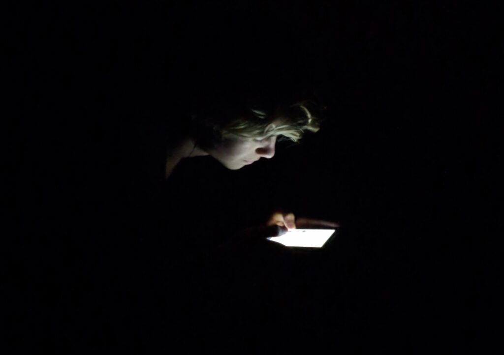 Photo of a face in the dark illuminated by the light of their phone screen