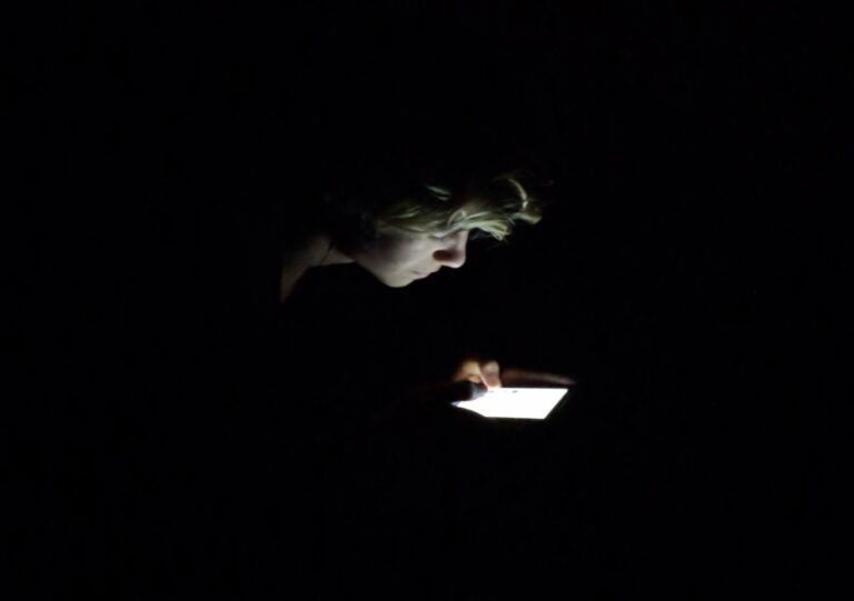 Photo of a face in the dark illuminated by the light of their phone screen
